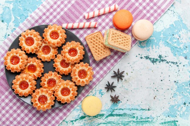 Draufsicht köstliche kleine Kekse mit Orangenmarmeladen-Macarons und Waffeln auf dem blauen Schreibtischkekskeks süßer Zuckerfarbentee