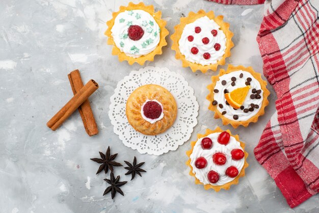 Draufsicht köstliche kleine Kuchen mit Sahne und rotem Fruchtzimt auf dem hellen Schreibtischfruchtsüß