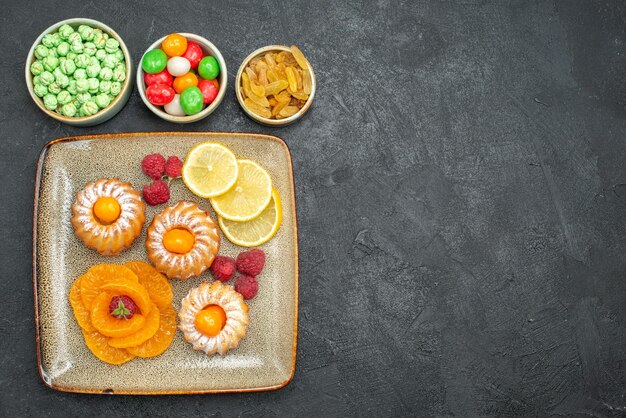 Draufsicht köstliche kleine Kuchen mit Zitronenscheiben, Mandarinen und Bonbons auf dunklem Hintergrund Tee-Frucht-Keks süßer Kekskuchen