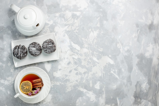 Draufsicht köstliche kleine Kuchen mit Zuckerguss und Tasse Tee auf dem hellweißen Hintergrundteekekskuchen backen Zuckersüßkuchen