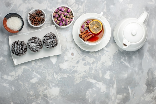 Draufsicht köstliche kleine Kuchen mit Zuckerguss und Tasse Tee auf hellweißem Hintergrund Tee-Kekskuchen backen Zucker süße Kuchenplätzchen