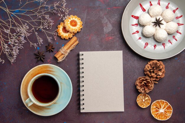Draufsicht köstliche Kokosbonbons klein und rund geformt mit einer Tasse Tee auf dunklem Hintergrund Kokossüßigkeit süßer Kuchenkeks