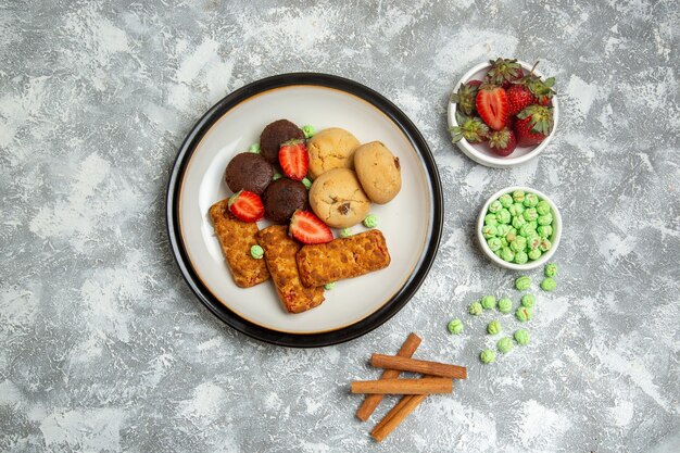 Draufsicht köstliche Kuchen mit Keksen Bonbons und Erdbeeren auf weißem Hintergrund Keks Zuckerkuchen süßen Kuchen Tee Keks