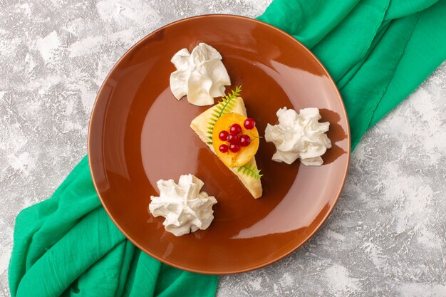 Draufsicht köstliche Kuchenscheibe mit Aprikose innerhalb brauner Platte mit Sahne auf dem hellen Schreibtischkuchenkeks süßer Teigauflauf