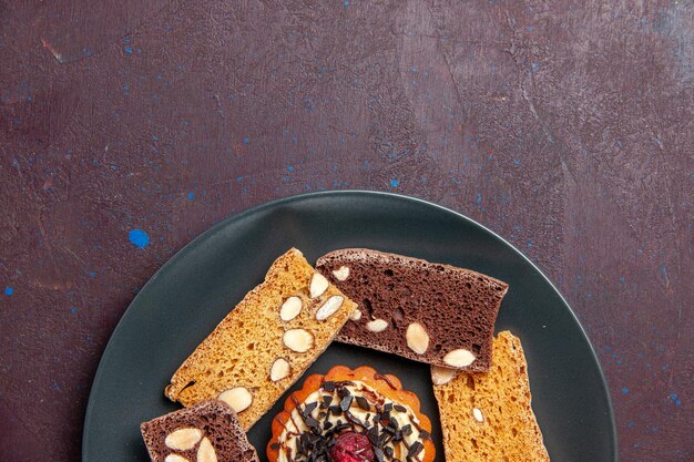 Draufsicht köstliche Kuchenscheiben mit Nüssen und kleinem Keks auf dunklem Hintergrund süßer Keksplätzchen-Dessertkuchen