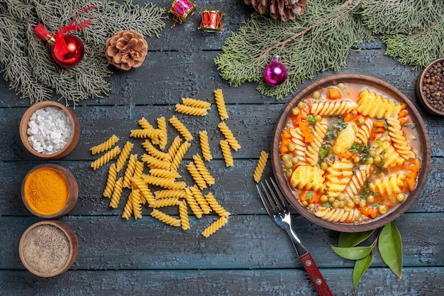 Draufsicht köstliche Nudelsuppe aus spiralförmiger italienischer Pasta mit Gewürzen auf dem dunkelblauen Schreibtischgericht Küche Farbsuppe Pasta