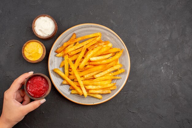 Draufsicht köstliche Pommes frites mit Gewürzen auf dunklem Hintergrund Kartoffelmahlzeit Fast-Food-Gericht Burger