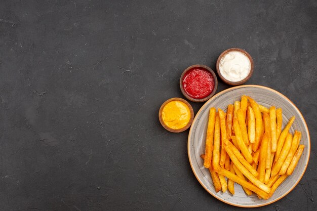 Draufsicht köstliche Pommes frites mit Gewürzen auf dunklem Hintergrund Mahlzeit Kartoffel-Fast-Food-Burger-Gericht