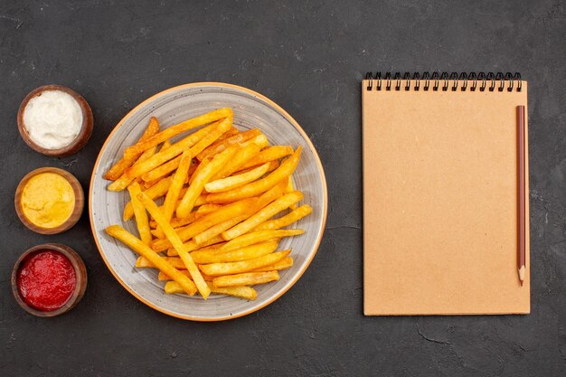 Draufsicht köstliche Pommes Frites mit Gewürzen auf dunklem Schreibtisch Kartoffelmahlzeit Burger Fastfood