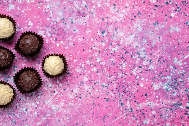 Draufsicht köstliche Pralinen weiße und dunkle Schokolade auf rosa Schreibtisch.