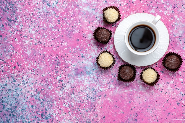 Draufsicht köstliche Pralinen weiße und dunkle Schokolade mit Tasse Tee auf dem rosa Hintergrund.
