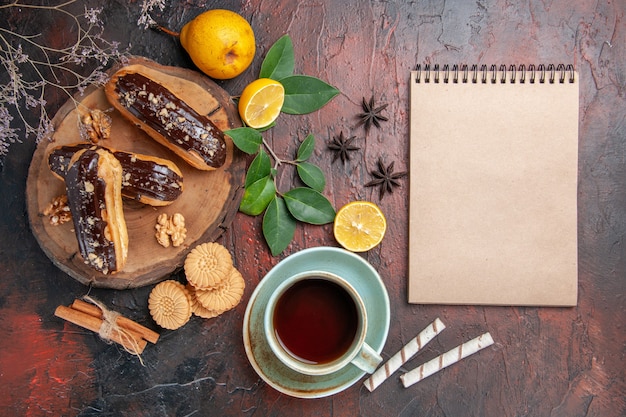 Draufsicht köstliche Schoko-Eclairs mit Tasse Tee auf dunklem Tischdessert-Süßigkeiten-Kuchen