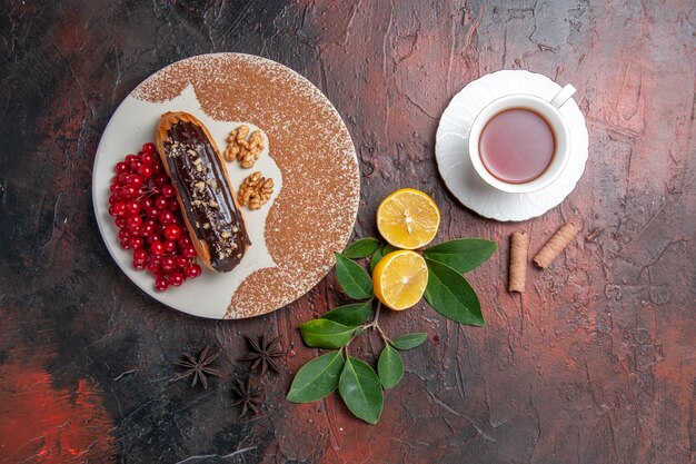 Draufsicht köstliche Schoko-Eclairs mit Tasse Tee auf dunklem Tischkuchen-Dessertkuchen süß