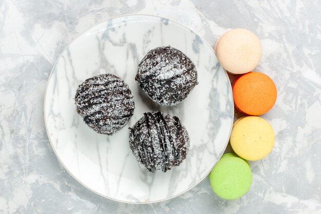 Draufsicht köstliche Schokoladenbällchen runde geformte Kuchen mit Zuckerguss und Macarons auf hellweißem Schreibtisch backen Kuchen Schokoladenzuckerkuchen süß