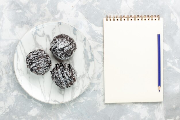 Draufsicht köstliche Schokoladenbällchen runde geformte Kuchen mit Zuckerguss und Notizblock auf hellweißem Schreibtisch backen Kuchen Schokoladenzuckerkuchen süß