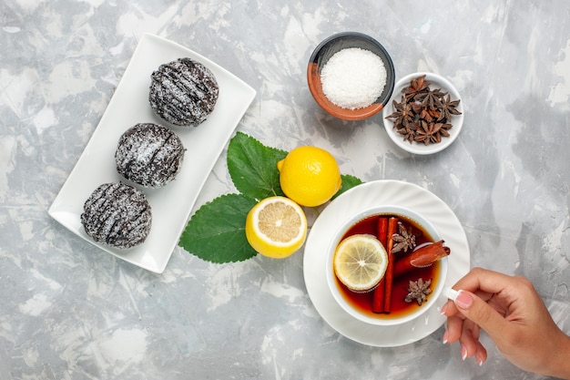 Draufsicht köstliche Schokoladenkuchen kleine Runde gebildet mit Zitrone und Tasse Tee auf weißer Oberfläche Obstkuchen Keks süßer Zucker backen Keks