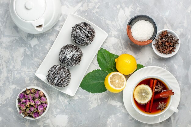 Draufsicht köstliche Schokoladenkuchen kleine Runde gebildet mit Zitrone und Tasse Tee auf weißer Oberfläche Obstkuchen Keks süßer Zucker backen Keks