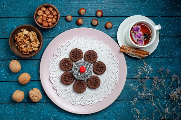 Draufsicht köstliche Schokoladenplätzchen mit Nüssen und Tasse Tee auf blauem rustikalem Schreibtischkeks-Tee-Keks süßem Kuchenzucker