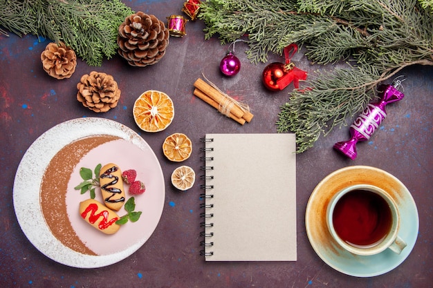 Draufsicht köstliche süße kekse mit tasse tee und weihnachtsbaum auf dunklem hintergrund cookie süßer keks zuckerfarbe kuchen