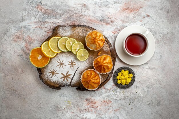 Draufsicht köstliche süße Kuchen mit Zitronenscheiben und Tasse Tee auf weißer Oberfläche