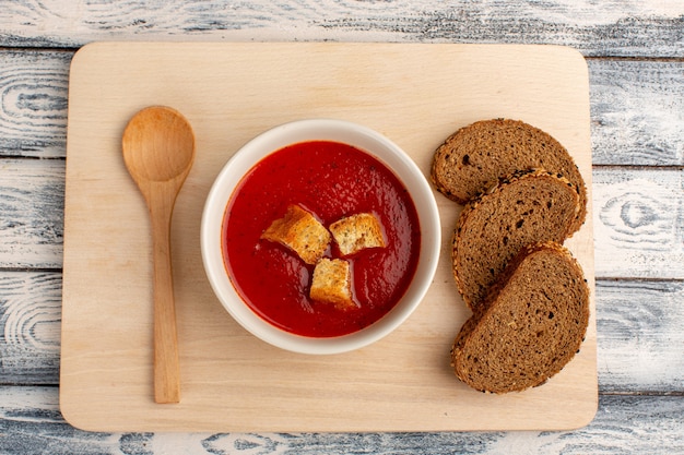 Draufsicht köstliche Tomatensuppe mit dunklen Brotlaibs auf dem grauen Tisch, Suppenessen Mahlzeit Abendessen