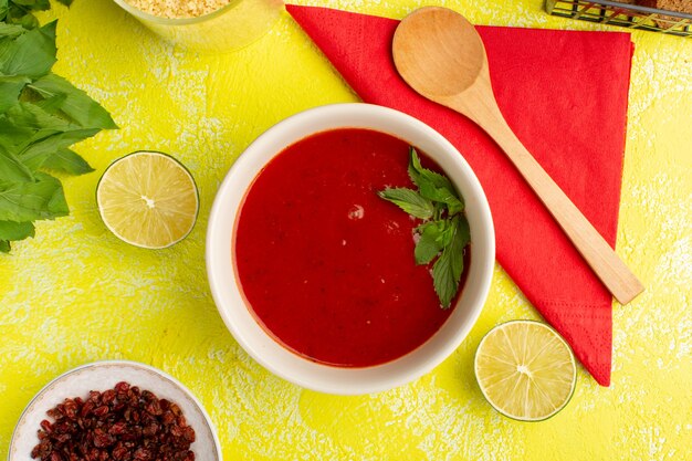 Draufsicht köstliche Tomatensuppe mit Grün und Zitrone auf dem gelben Tisch, Suppenmahlzeitabendessengemüse