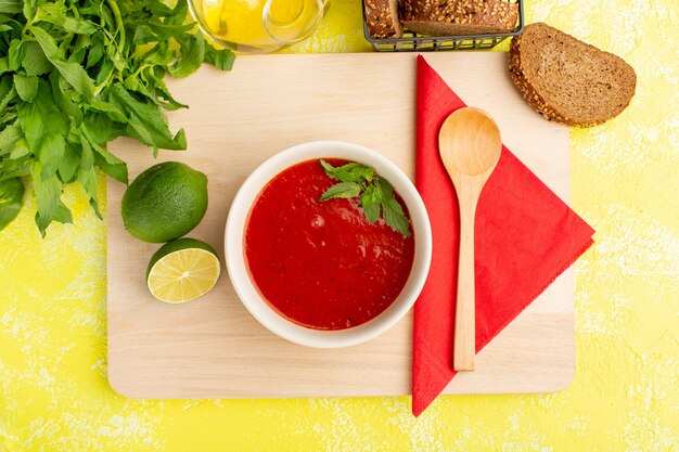 Draufsicht köstliche Tomatensuppe mit Zitrone und Grün auf gelbem Tisch, Suppenessen Mahlzeit Abendessen