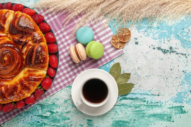 Draufsicht köstliche Torte mit Erdbeer-Macarons und Tasse Tee auf der blauen Oberfläche