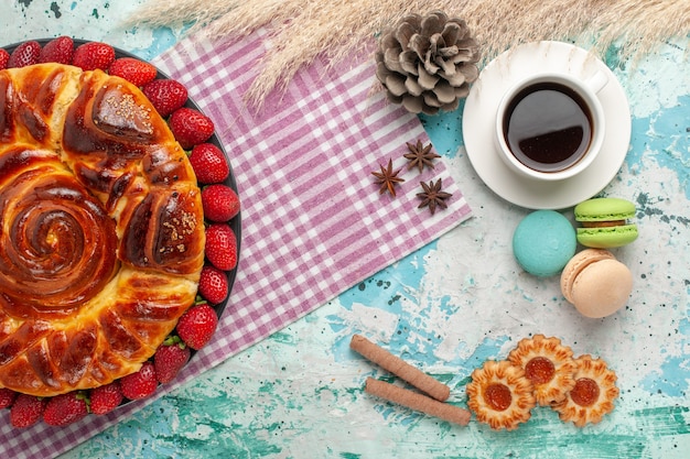 Draufsicht köstliche torte mit frischen roten erdbeeren macarons und tasse tee auf der blauen oberfläche