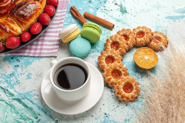 Draufsicht köstliche Torte mit frischen roten Erdbeeren Macarons und Tasse Tee auf hellblauer Oberfläche