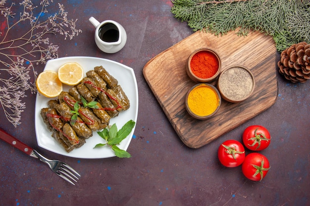 Draufsicht köstlicher Blattdolma mit Zitronenscheiben und Gewürzen auf dunklem Hintergrund