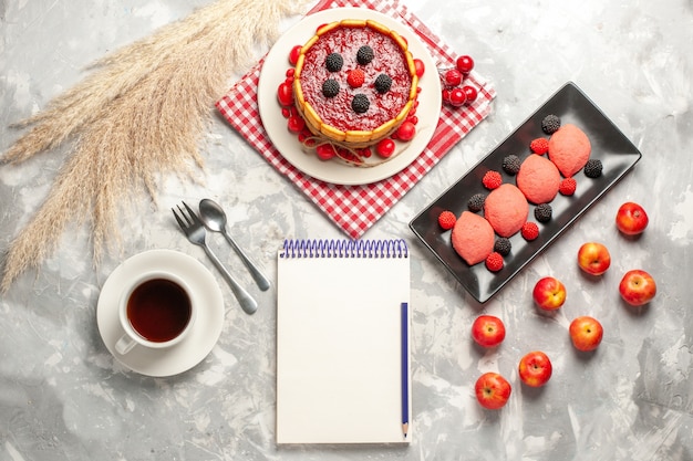 Draufsicht köstlicher cremiger Kuchen mit roter Zuckerglasur und Crackern zusammen mit einer Tasse Tee auf weißem Oberflächenkuchenkeks süßer Obstkuchenplätzchen