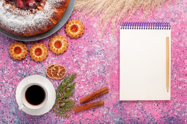 Draufsicht köstlicher Erdbeerkuchenzuckerpulverkuchen mit Keksnotizblock und Tasse Tee auf rosa Hintergrundkuchen süßer Zuckerplätzchenkuchen