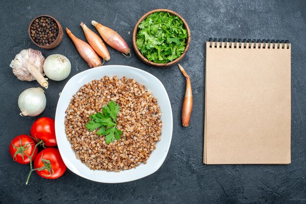 Draufsicht köstlicher gekochter Buchweizen mit Tomaten und Grüns auf grauem Schreibtisch