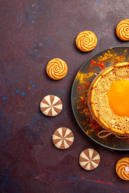 Kostenloses Foto draufsicht köstlicher gelber kuchen cremiges dessert mit keksen auf dem dunklen schreibtisch