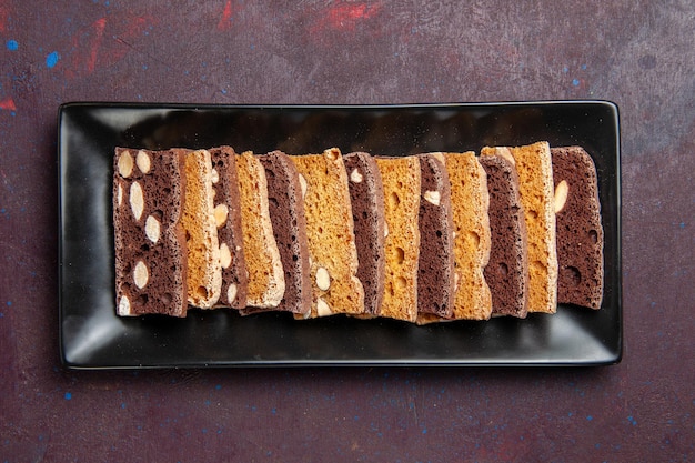 Draufsicht köstlicher geschnittener Kuchen mit Nüssen in der Kuchenform auf dunklem Hintergrund süßer Kakaoteigkuchen-Kekskuchen-Zucker
