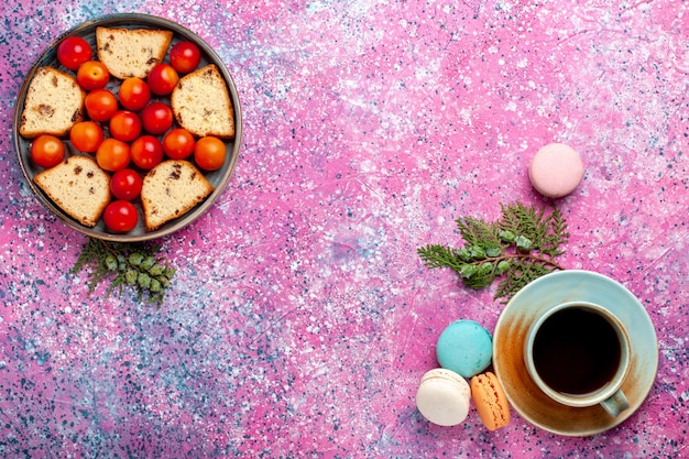 Draufsicht köstlicher geschnittener Kuchen mit sauren frischen Pflaumen Macarons und Tee auf rosa Schreibtisch