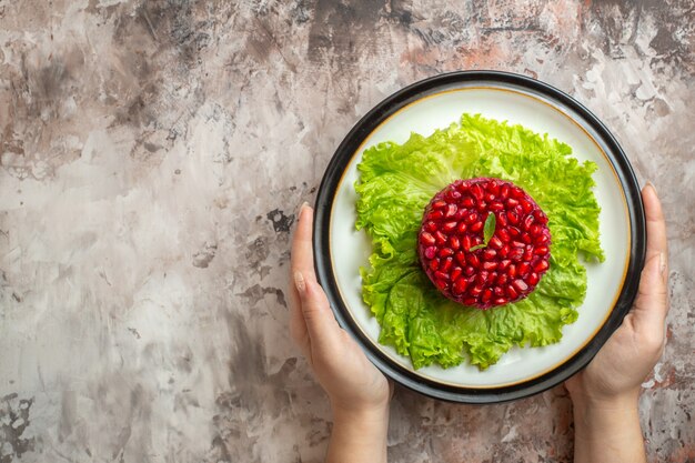 Draufsicht köstlicher Granatapfelsalat rund auf grünem Salat auf hellem Hintergrund