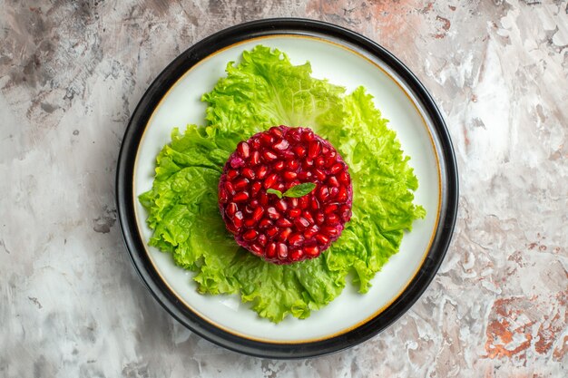 Draufsicht köstlicher Granatapfelsalat rund auf grünem Salat auf hellem Hintergrund