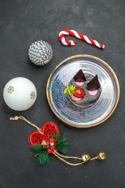 Draufsicht köstlicher Käsekuchen mit Erdbeere und Schokolade auf ovalem Teller Weihnachtsbaumspielzeug auf dunklem, isoliertem Hintergrund