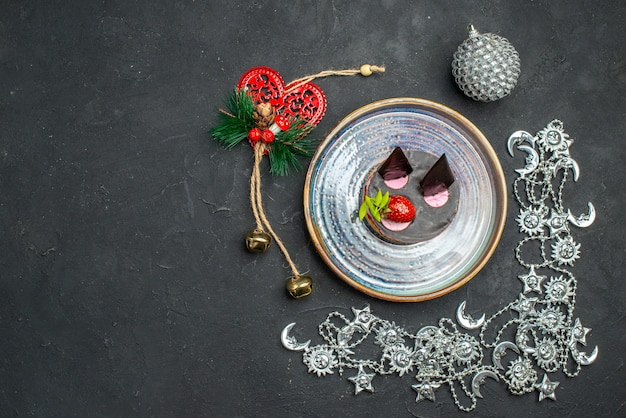 Draufsicht köstlicher käsekuchen mit erdbeere und schokolade auf ovalen silbernen weihnachtsornamenten auf dunklem, isoliertem hintergrund