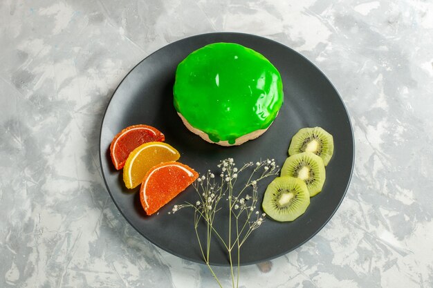 Draufsicht köstlicher kleiner Kuchen mit grünem Zuckerguss innerhalb Platte auf weißem Oberflächenkuchen bisciut süßer Zuckerkuchen