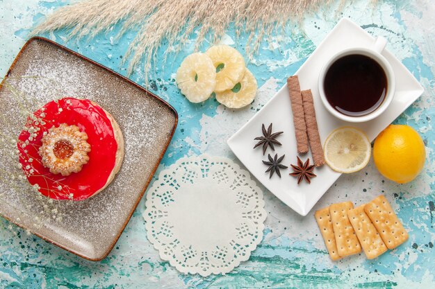 Draufsicht köstlicher kleiner Kuchen mit roten Sahnecrackern und Tasse Tee auf dem blauen Hintergrundplätzchen süßer Kekszuckerkuchen-Kuchen-Tee