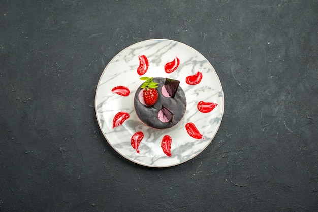 Draufsicht köstlicher kuchen mit erdbeere und schokolade auf ovalem teller auf dunklem hintergrund