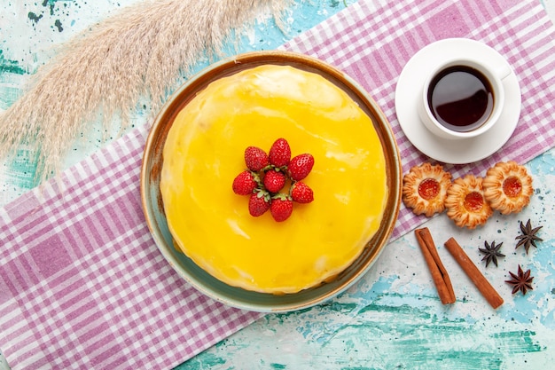 Kostenloses Foto draufsicht köstlicher kuchen mit gelben sirup frischen roten erdbeeren und tasse tee auf blauer oberfläche kekskuchen backen süßen zucker kuchen tee keks