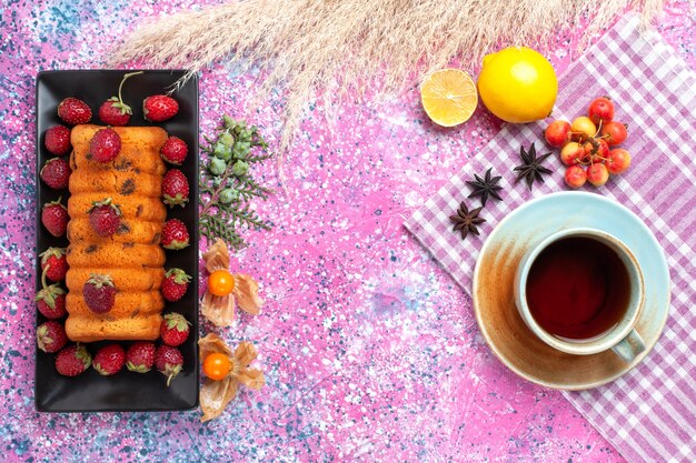 Draufsicht köstlicher Kuchen mit rotem frischem Erdbeertee und Zitrone auf dem rosa Schreibtisch.