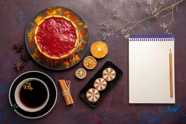 Draufsicht köstlicher kuchen mit roten sahnekeksen und tasse kaffee auf dunklem schreibtischkekskuchen zuckerdessertkuchen süße kekse