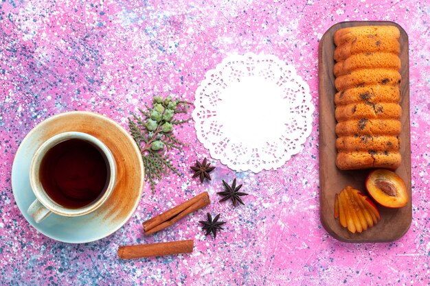 Draufsicht köstlicher Kuchen süß und lecker mit Pflaumen und einer Tasse Tee auf dem rosa Schreibtisch.