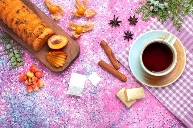 Draufsicht köstlicher Kuchen süß und lecker mit Pflaumentasse Tee und süßen Kirschen auf rosa Schreibtisch.