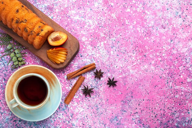 Draufsicht köstlicher Kuchen süß und lecker mit Pflaumentee auf dem rosa Schreibtisch.